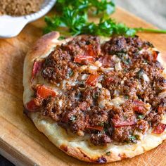 a pizza sitting on top of a wooden cutting board next to a bowl of seasoning