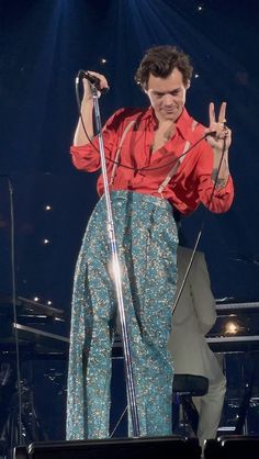 a man standing on stage with a microphone and peace sign in front of his hand