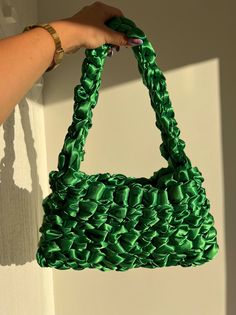 a hand holding a green purse on top of a white wall