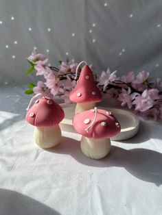 three little pink mushrooms sitting on top of a white plate next to some purple flowers