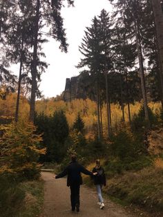 a man and woman walking down a path in the woods with trees on both sides