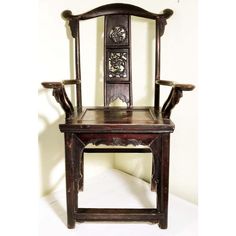 an old wooden chair with carvings on the armrests and back rests against a white wall