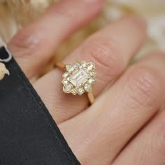 a woman's hand holding a ring with an emerald and diamond center stone on it