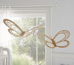 a baby crib in front of a window with a butterfly mobile hanging from it's side