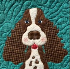 a brown and white dog is on a blue quilted wall hanging with it's tongue out