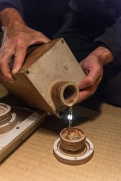 a man pouring water into a wooden container on top of a table next to a stove