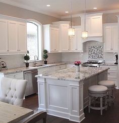 a large kitchen with white cabinets and marble counter tops, along with an island in the middle