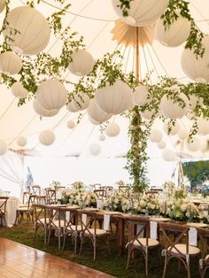 a large tent with tables, chairs and paper lanterns hanging from the ceiling