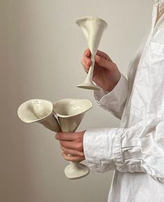 a person holding three white cups and saucers in one hand while another holds the other