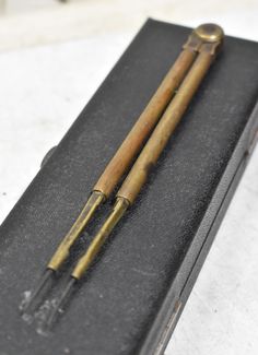 two antique brass - plated metal items in a black box on a white surface