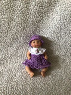 a doll is laying on the floor wearing a purple dress and hat with white ruffles