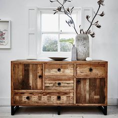 a wooden dresser with two vases on top of it next to a white wall