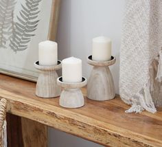 three white candles sitting on top of a wooden table next to a framed photo and mirror