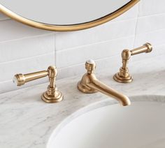 a bathroom sink with two faucets in front of a mirror and marble counter top