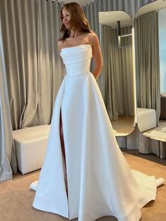 a woman in a white wedding dress standing next to a mirror with her hand on her hip