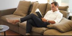 a man sitting on a couch with his feet up and reading a book in front of him