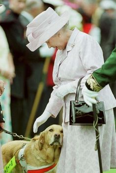 an older woman in white holding onto a dog on a leash while wearing a pink hat