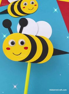 two paper bees on top of a stick with eyes and antennae, one is yellow and the other is black