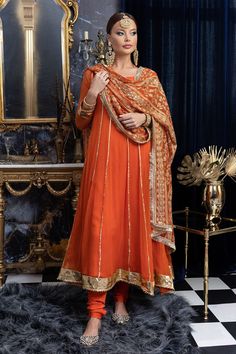 Apricot Anarkali is the dress of queens and princes. It's regal and takes craftsmanship and effort to achieve an exquisite brew of tangerine and gold. Presenting 'Apricot' the exclusive Maria Nasir design that can be your next wedding outfit for the season. The beautiful gota and tilla work, hand-cut sequins, silk threadwork in gold fits beautifully in auburn chiffon silhouette. The round neck with deep back and gorgeous tassels make this ensemble extremely gorgeous. Gold bordered panels and gold foil gota lace in the bottom brings out the style exquisitely. Paired with similar hued churidaars and heavily embroidered dupatta in chiffon fabric is all you need to turn all the heads toward you! Top: Color: Orange Fabric: Chiffon Anarkali dress with gota work Round neck 3/4 sheer sleeves with Chiffon Anarkali Dress, Orange Dress Outfits, Chiffon Anarkali, Anarkali Designs, Silk Anarkali Suits, Bridal Suits, Orange Suit, Silk Anarkali, Designer Anarkali