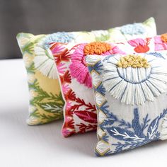 three decorative pillows on a white surface with one colorful flowered pillow in the middle