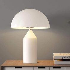 a white lamp sitting on top of a table next to a book case and plant