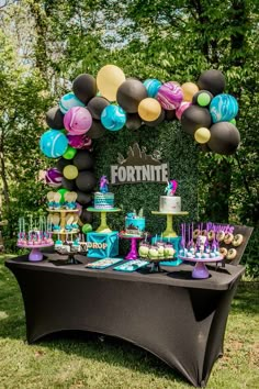 a table topped with cakes and desserts under a fortte sign surrounded by balloons