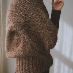 a woman in a brown sweater is holding her cell phone up to her ear and looking off into the distance