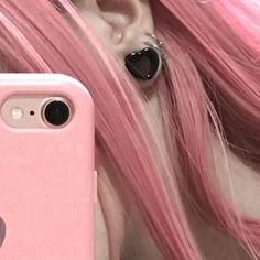 a girl with pink hair and piercings is looking at her phone