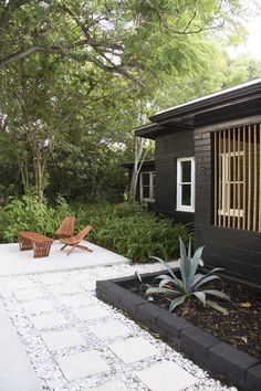 a wooden chair sitting in the middle of a garden next to a building and trees