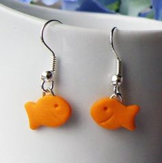 a pair of orange fish earrings sitting on top of a white cup