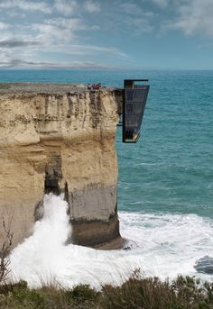 a man is hanging off the side of a cliff above the ocean with his feet in the water