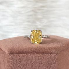 a yellow diamond ring sitting on top of a pink velvet box with white diamonds around it