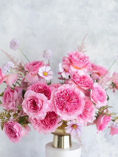 a white vase filled with pink flowers on top of a table