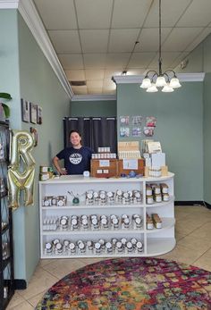 a man standing behind a counter with lots of items on it in front of a rug