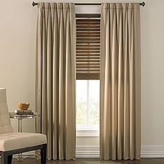 a white chair sitting in front of a window next to a window covered in curtains