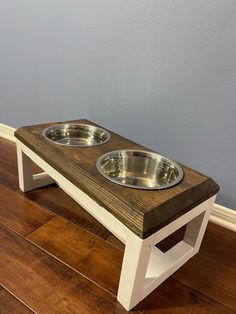 two dog bowls are on a wooden elevated pet table with white legs and brown top