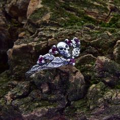 a skull ring sitting on top of a rock covered in green moss and purple stones