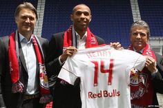 two men are holding up a red bulls jersey in front of an empty bleachers