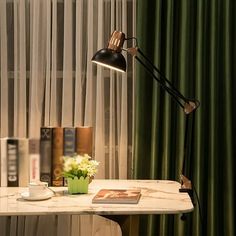 a desk lamp sitting on top of a white table next to a green curtained window