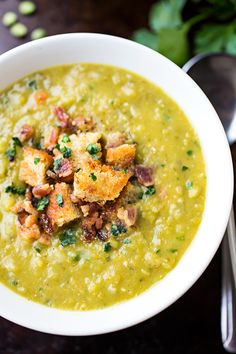 a white bowl filled with green soup and bread croutons on top of it