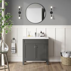 a white sink sitting under a round mirror next to a gray cabinet and counter top