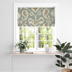 a window with a green and white patterned roman blind next to a potted plant