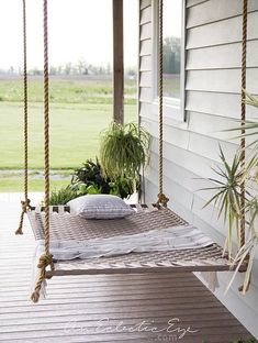 a porch swing with pillows and plants on it