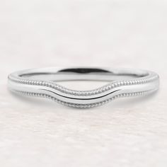 a white gold wedding band with beaded edges on a plain surface, ready to be worn