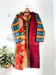 a colorful coat hanging on a wall next to a potted plant