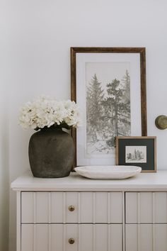 a vase with white flowers sitting on top of a dresser next to a framed photograph