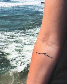 a woman's arm with a small tattoo on it, and the ocean in the background