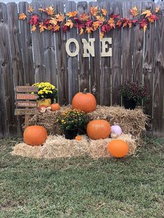 pumpkins and hay bales in front of a one sign on a wooden fence