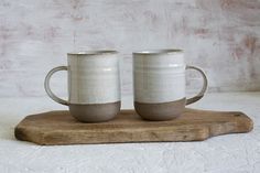 two mugs sitting on top of a wooden board