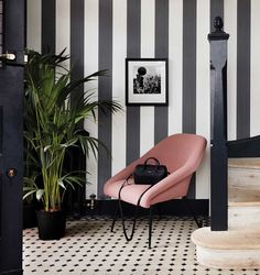 a black and white striped wall with a pink chair in the corner next to a potted plant